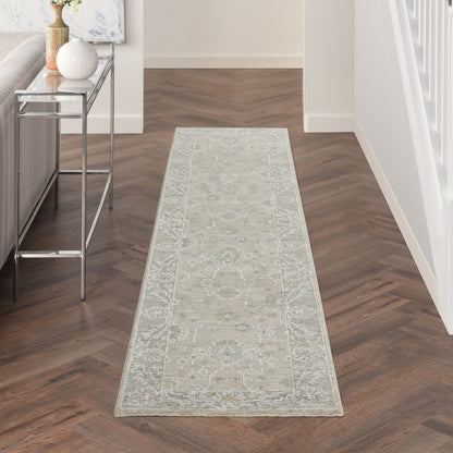 Vintage 10' runner rug in light gray with an ornate border, in a wood herringbone hallway; modern glass-topped console on the left.