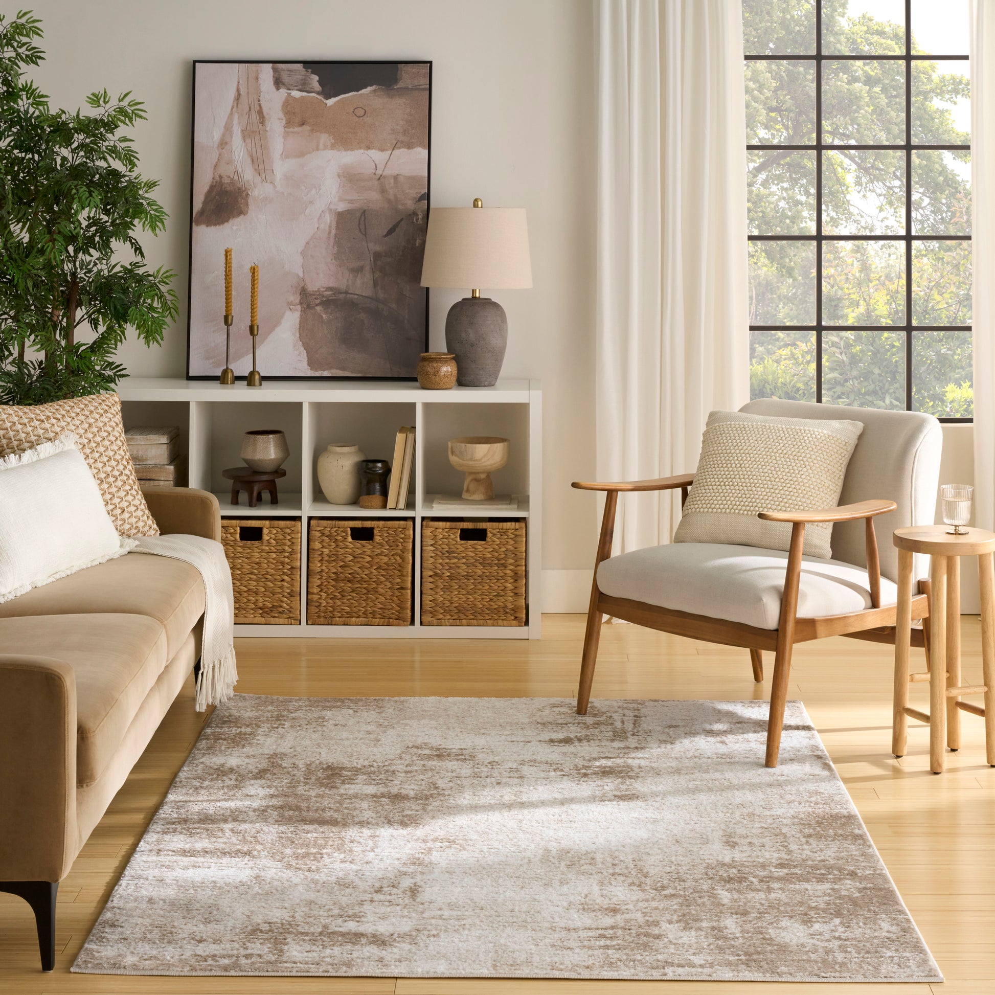 Neutral living room with beige sofa, mid-century wood chair, white cubby shelves, wicker baskets, abstract art, plant, and sunlit window.