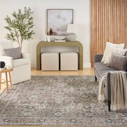 Cozy living room with olive-green console, beige ottomans, gray sofa, white armchair, tall plant, abstract art, and rug.