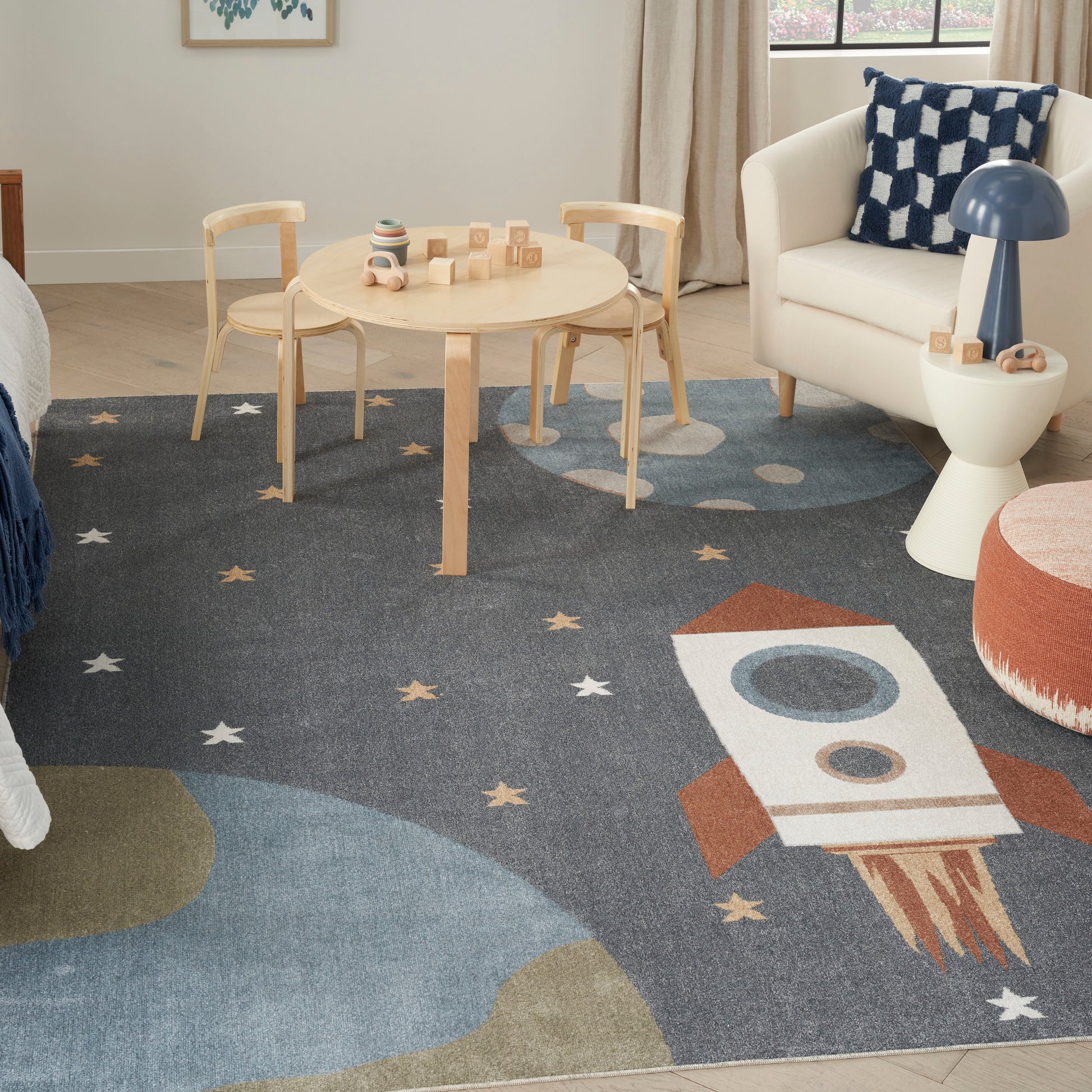 Space-themed kids rug, size 7' x 9', featuring a rocket, stars and planets; white armchair nearby.