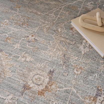 Soft blue-gray rug with beige and brown floral pattern; beige notebook and chunky wooden knot decor visible in the top-right.
