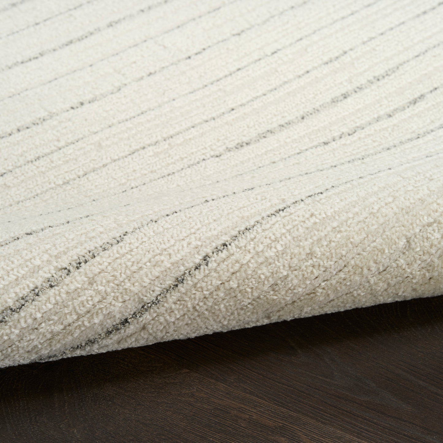 Cream area rug with light gray linear stripes, folded edge over dark wooden floor.
