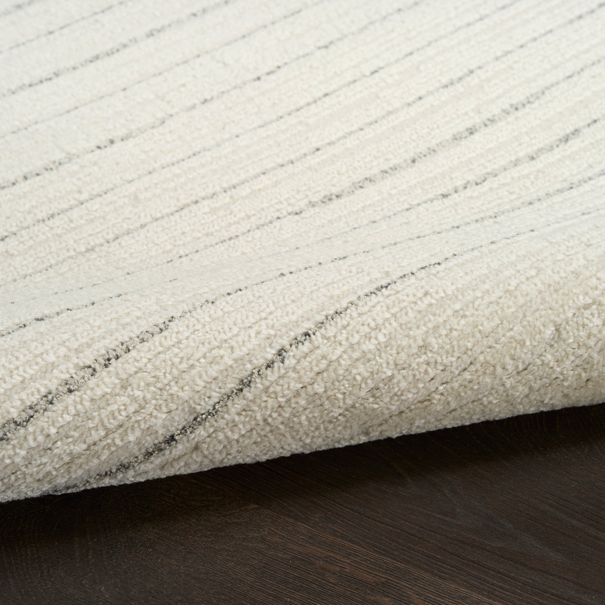Cream area rug with light gray linear stripes, folded edge over dark wooden floor.