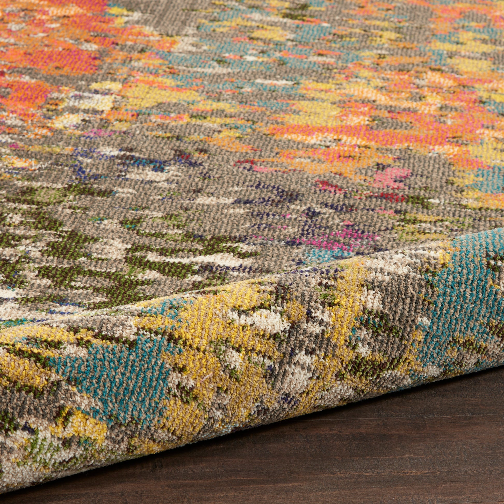 Vibrant multicolor abstract woven rug with geometric patterns, folded edge on dark wood floor.