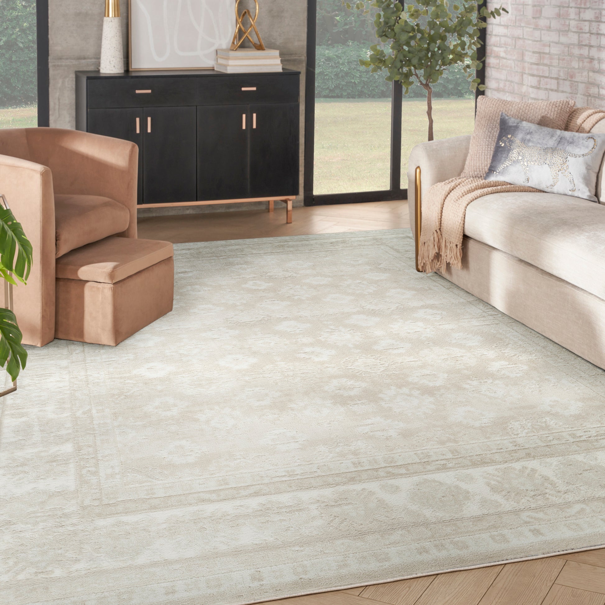 Rectangular cream-beige area rug with subtle border in a modern living room with tan sofa, peach chair, and black sideboard.