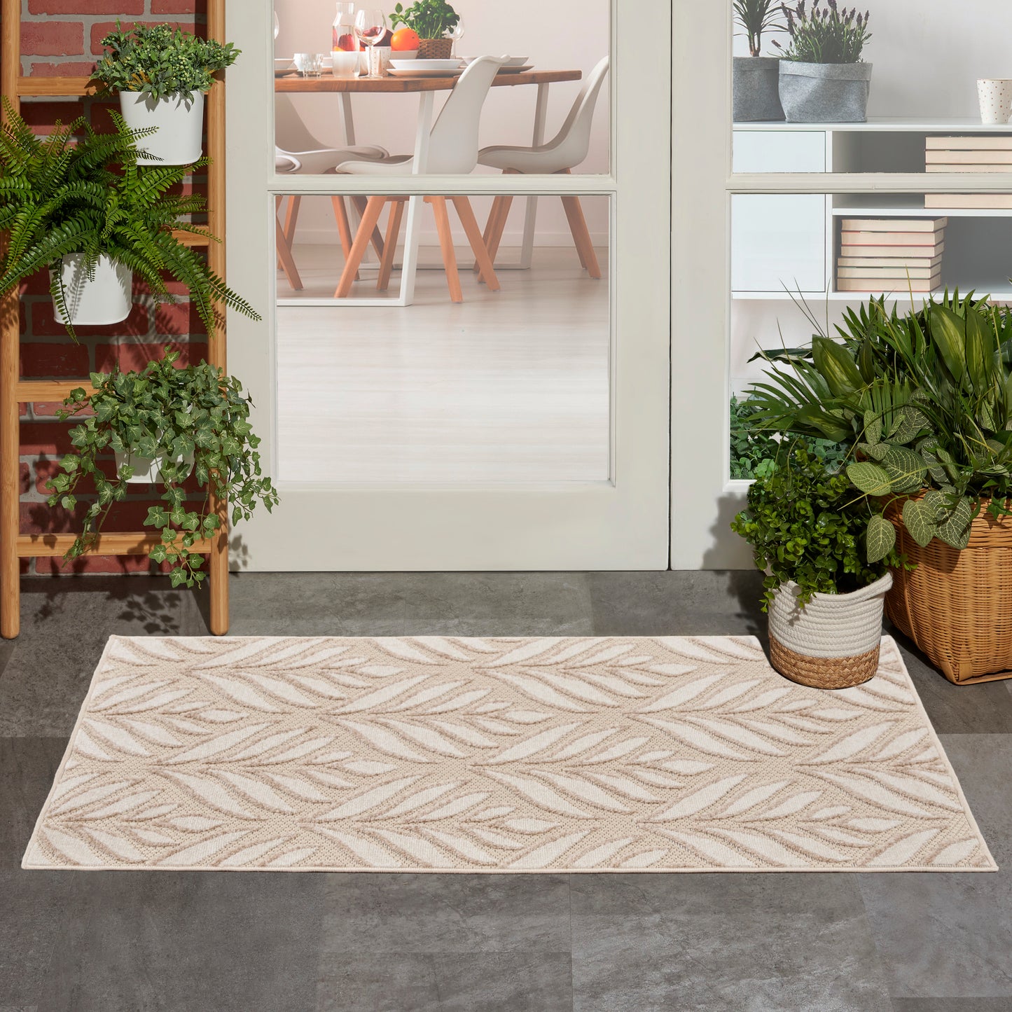 Rectangular beige area rug with tan palm-leaf pattern on entryway floor, with green plants and glass door to dining room.