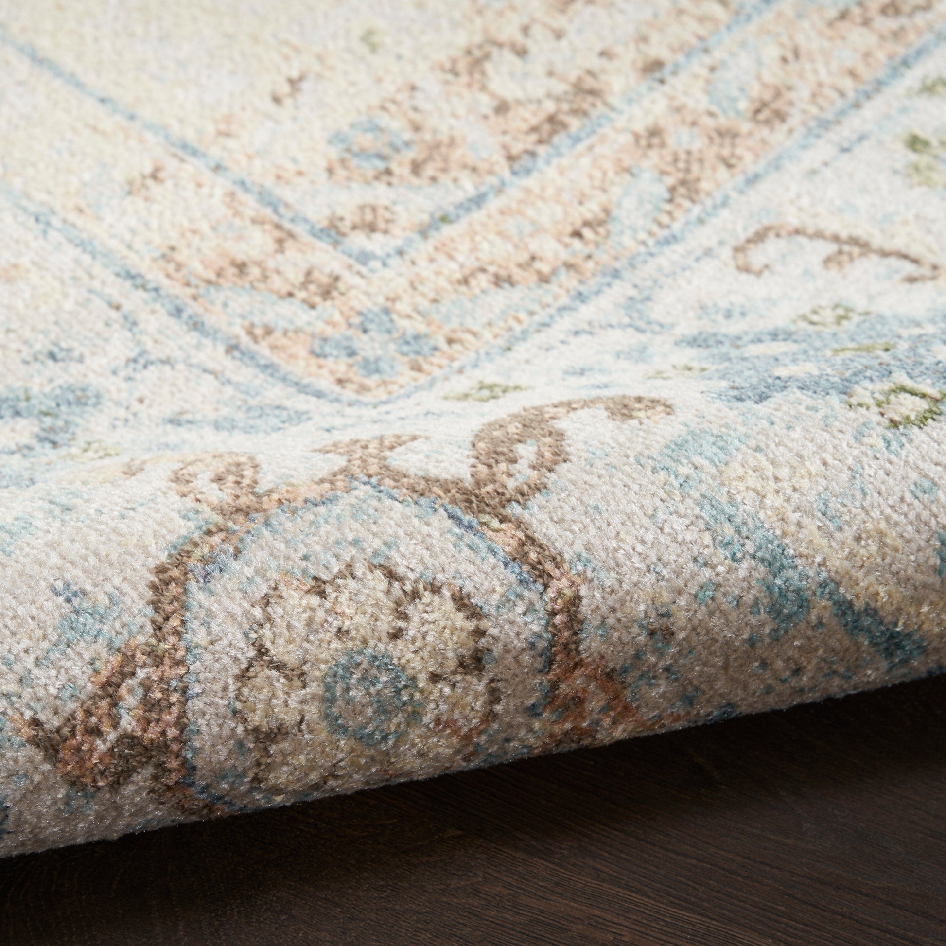 Close-up of a pastel blue and ivory woven rug with brown floral motifs and a folded edge.