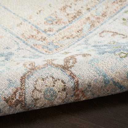 Close-up of a pastel blue and ivory woven rug with brown floral motifs and a folded edge.