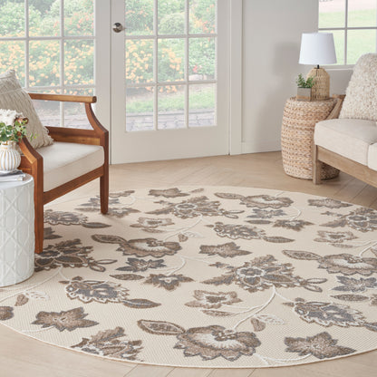 Round beige floral area rug with gray-brown flowers in a cozy neutral living room with wooden chairs and glass doors.