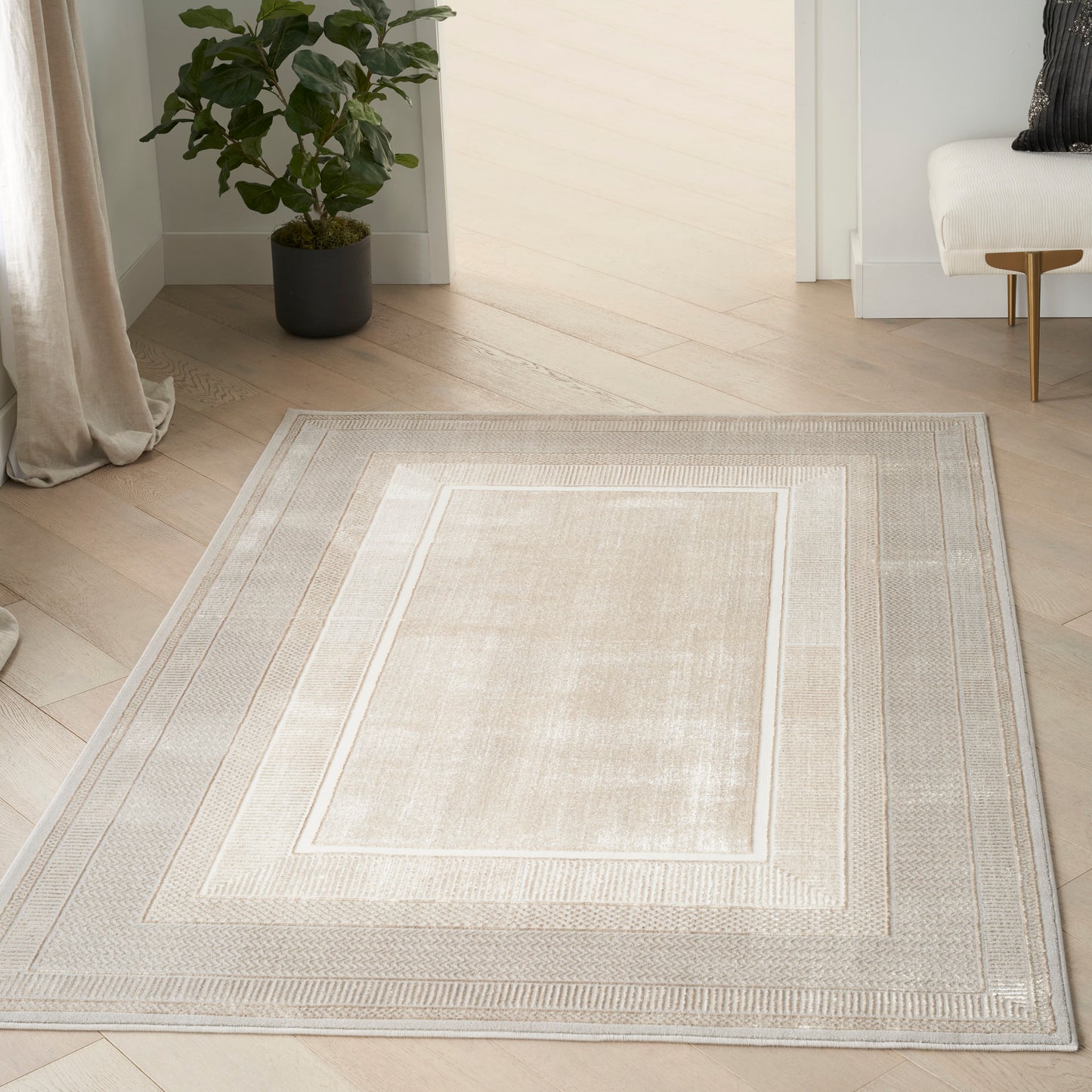 Beige rectangular area rug with nested borders in light taupe; soft, low-pile texture on light wood floor.