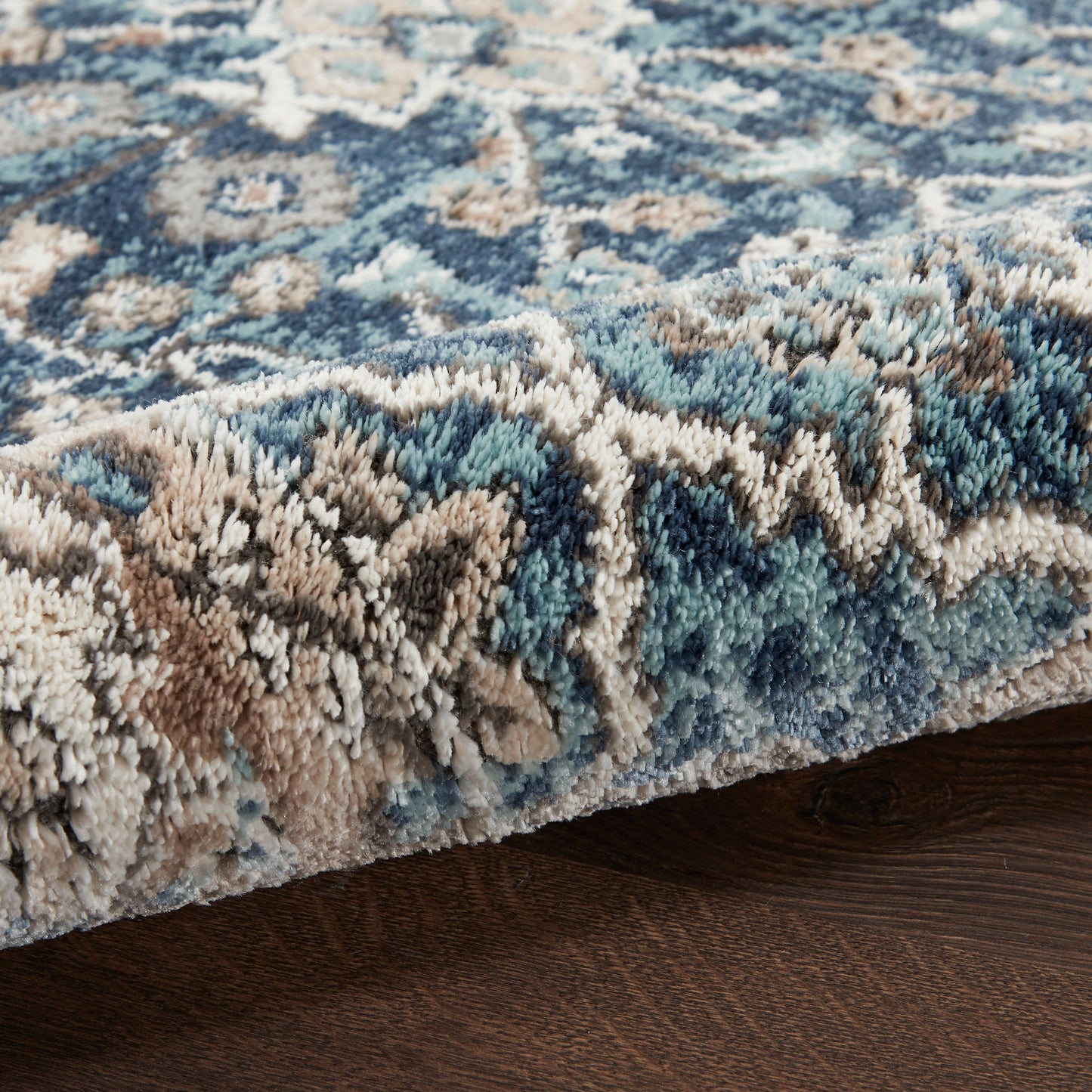 Close-up of a blue, beige and brown patterned shag rug with a plush pile on dark wood floor.