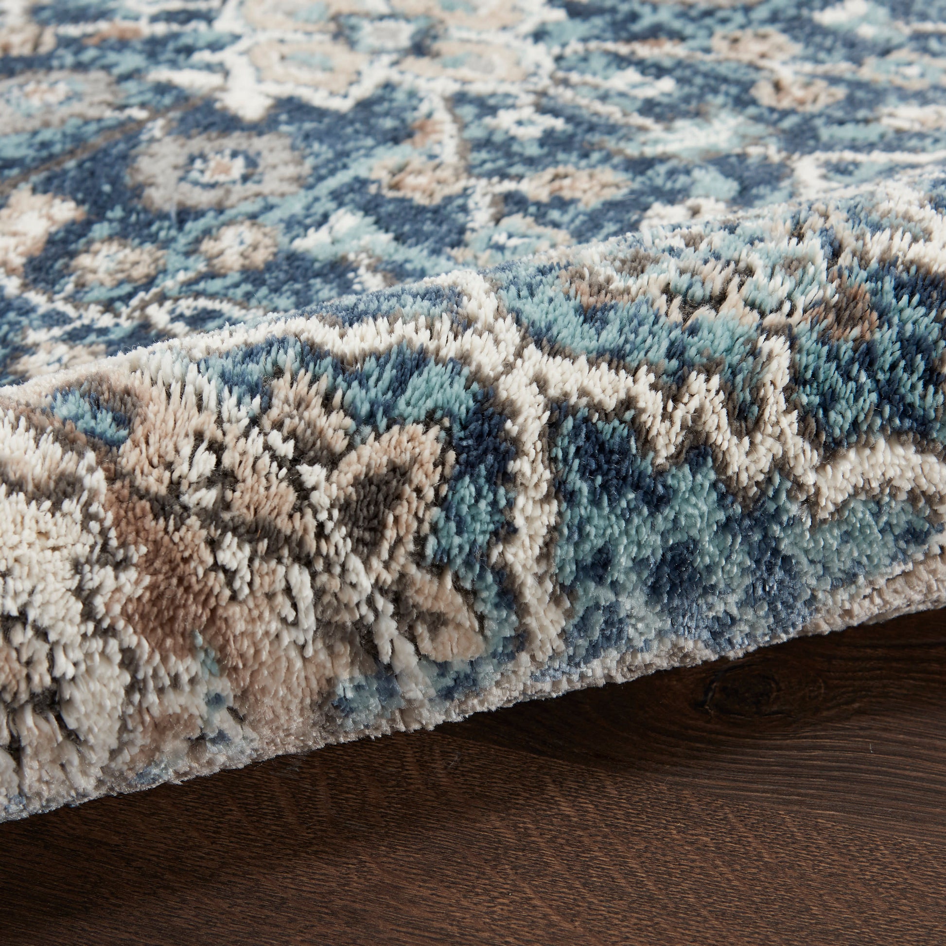 Close-up of a blue, beige and brown patterned shag rug with a plush pile on dark wood floor.