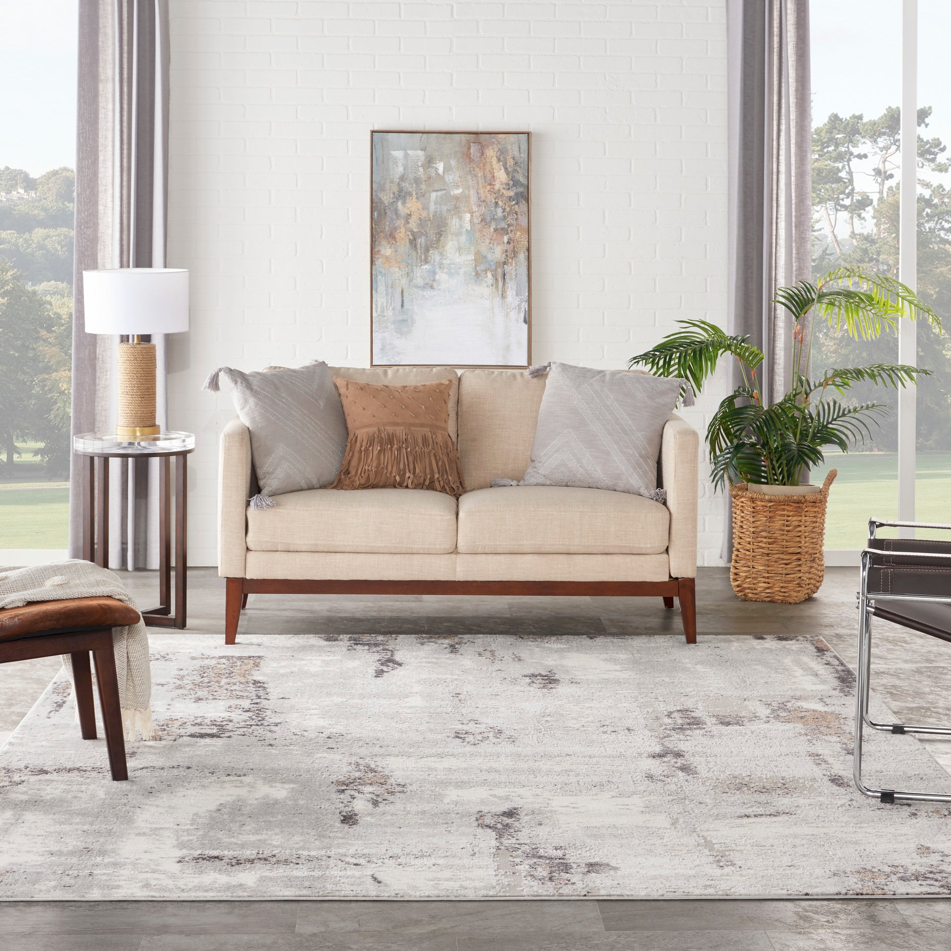 Beige mid-century sofa, wood legs, grey/tan cushions, abstract art, wicker plant basket, modern lamp, light rug.