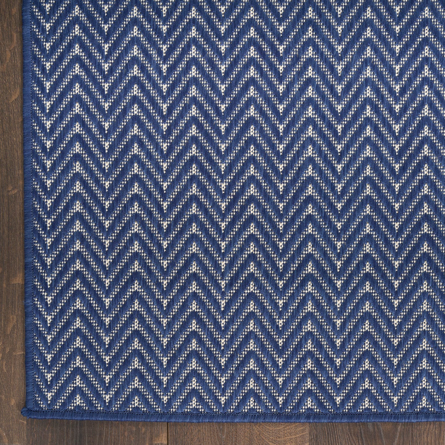 Blue chevron patterned rug with cream specks on dark indigo, woven texture, edge-bound, lying on wood floor.