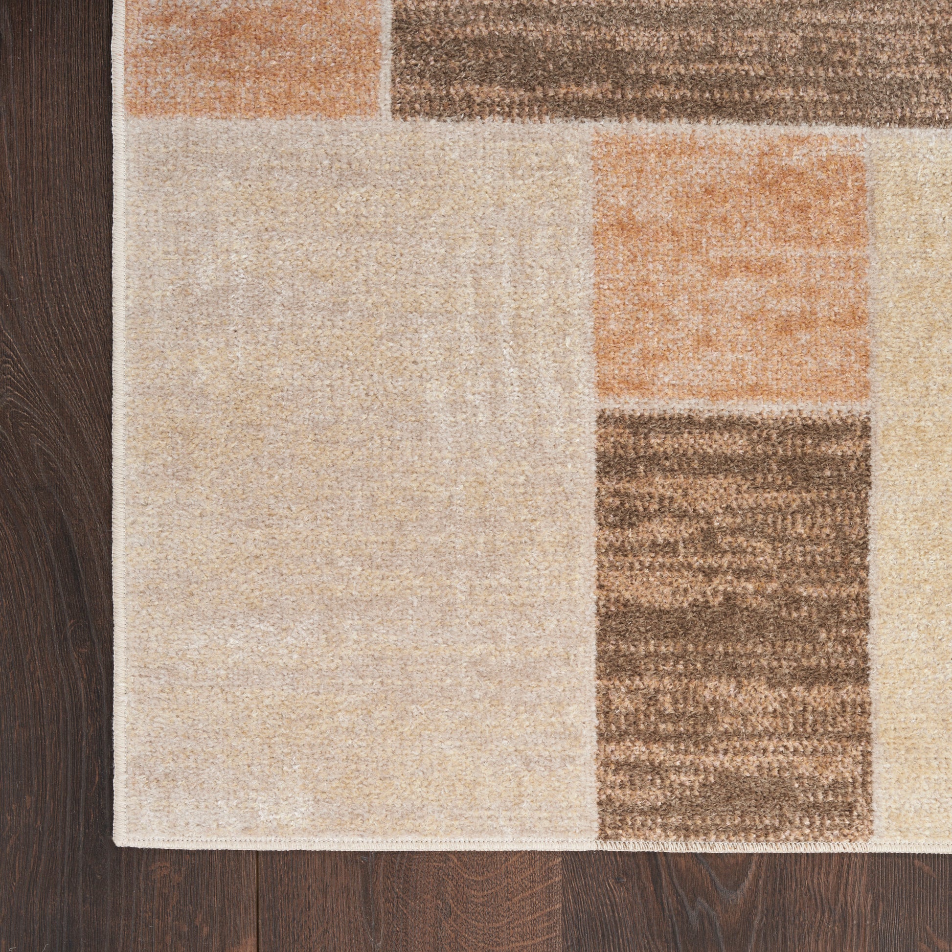Beige area rug with peach and brown geometric blocks on dark wood floor.