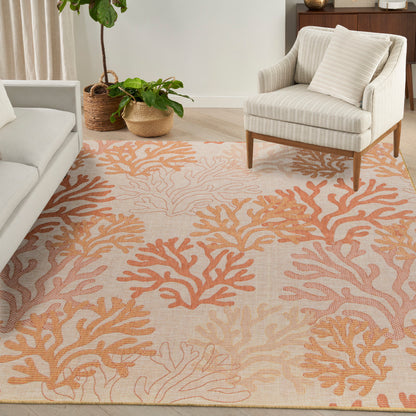 Cream sofa and striped beige armchair over a peach coral-pattern rug in a bright living room with woven wicker plant baskets.
