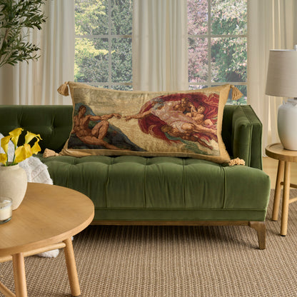 Green velvet tufted sofa with a long, fringed tapestry pillow, wooden round coffee table, beige rug, soft window light.