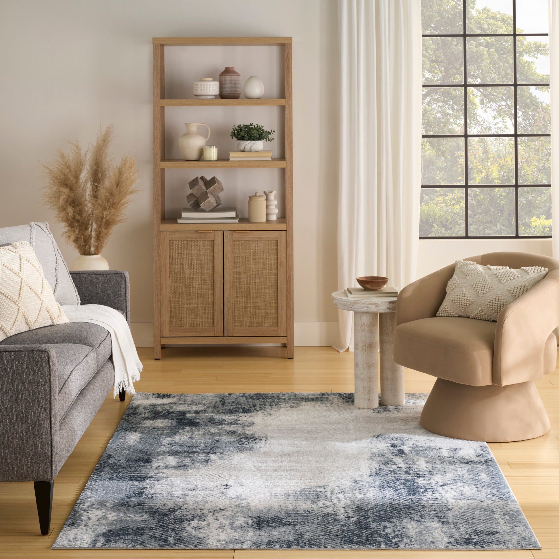 Warm living room with tall wooden shelf (woven doors), gray sofa, beige curved chair, and a blue abstract rug.