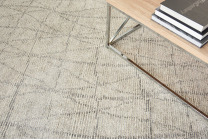 Beige area rug with a subtle diamond pattern and a modern light-wood coffee table with metal legs and stacked books.