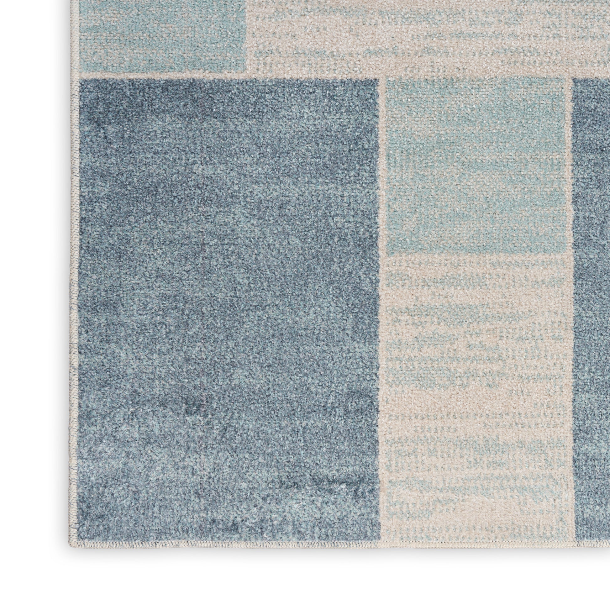 Geometric patchwork rug in blue and beige tones with denim and light blue squares; soft woven texture.