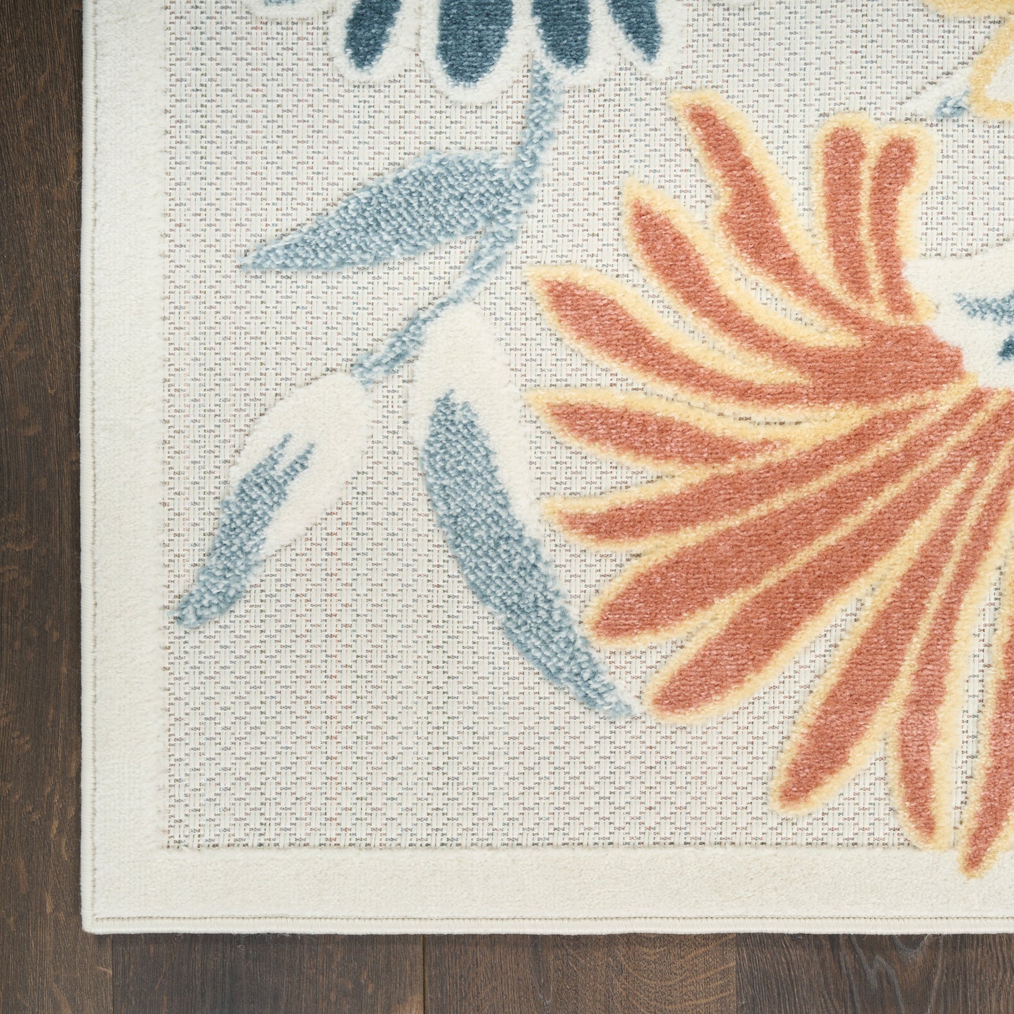 Cream outdoor rug with a bold orange flower and blue-green leaves, bordered edge, on dark wood floor.