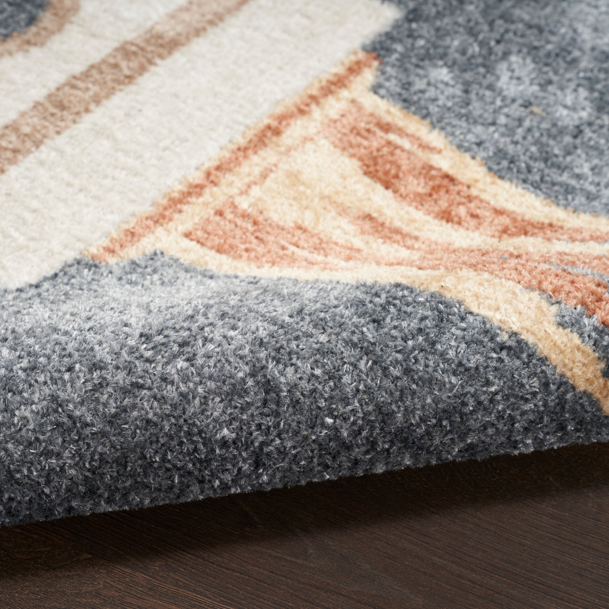 Close-up of a tufted area rug in blue & peach & cream geometric pattern with a folded edge.