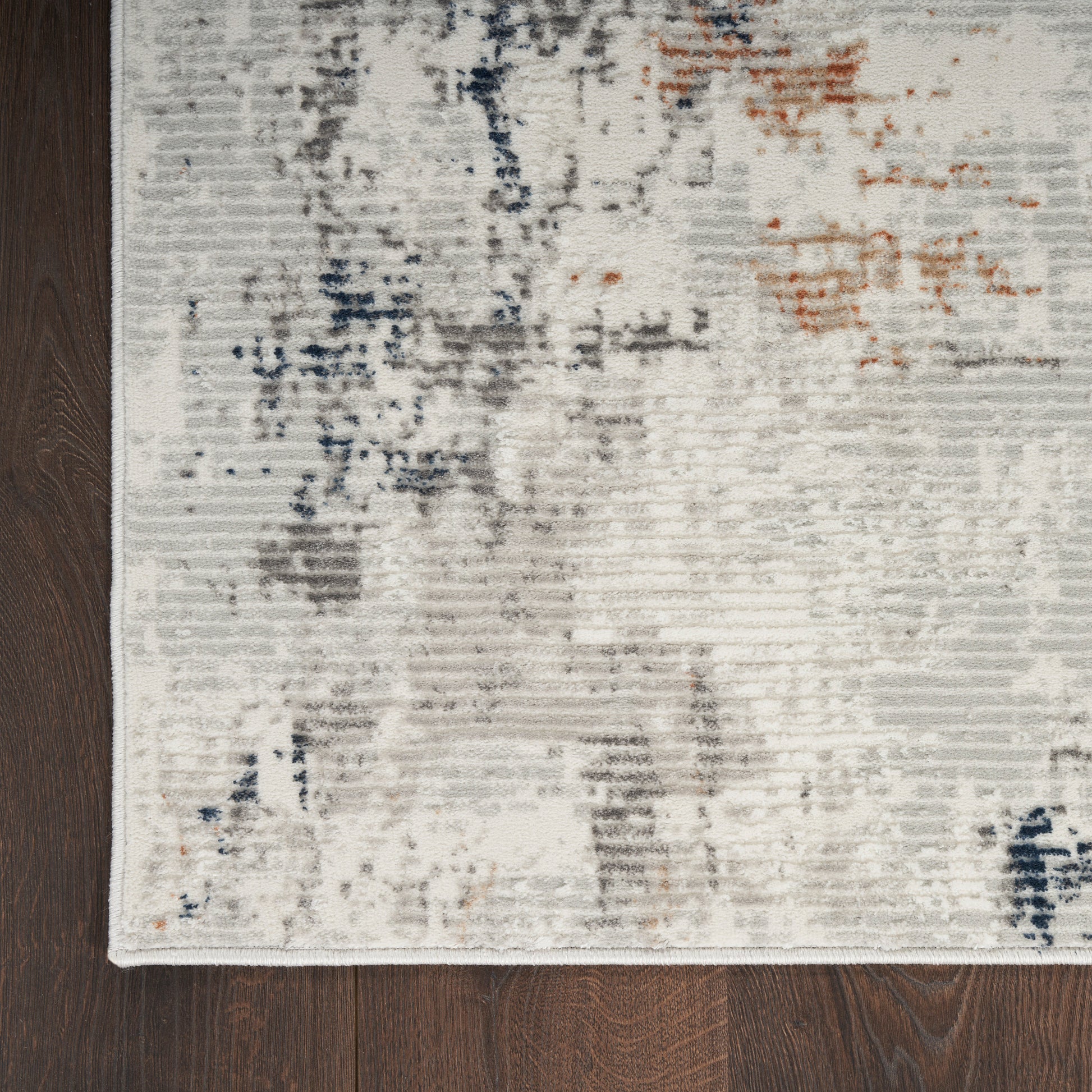 Cream and gray abstract area rug with blue and orange accents on dark wood floor.