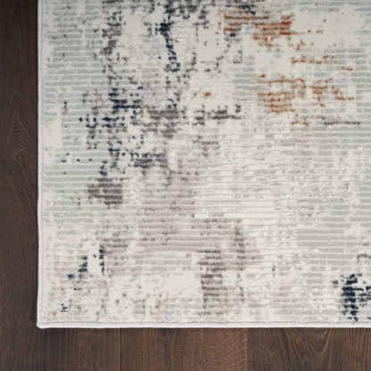 Cream and gray abstract area rug with blue and orange accents on dark wood floor.
