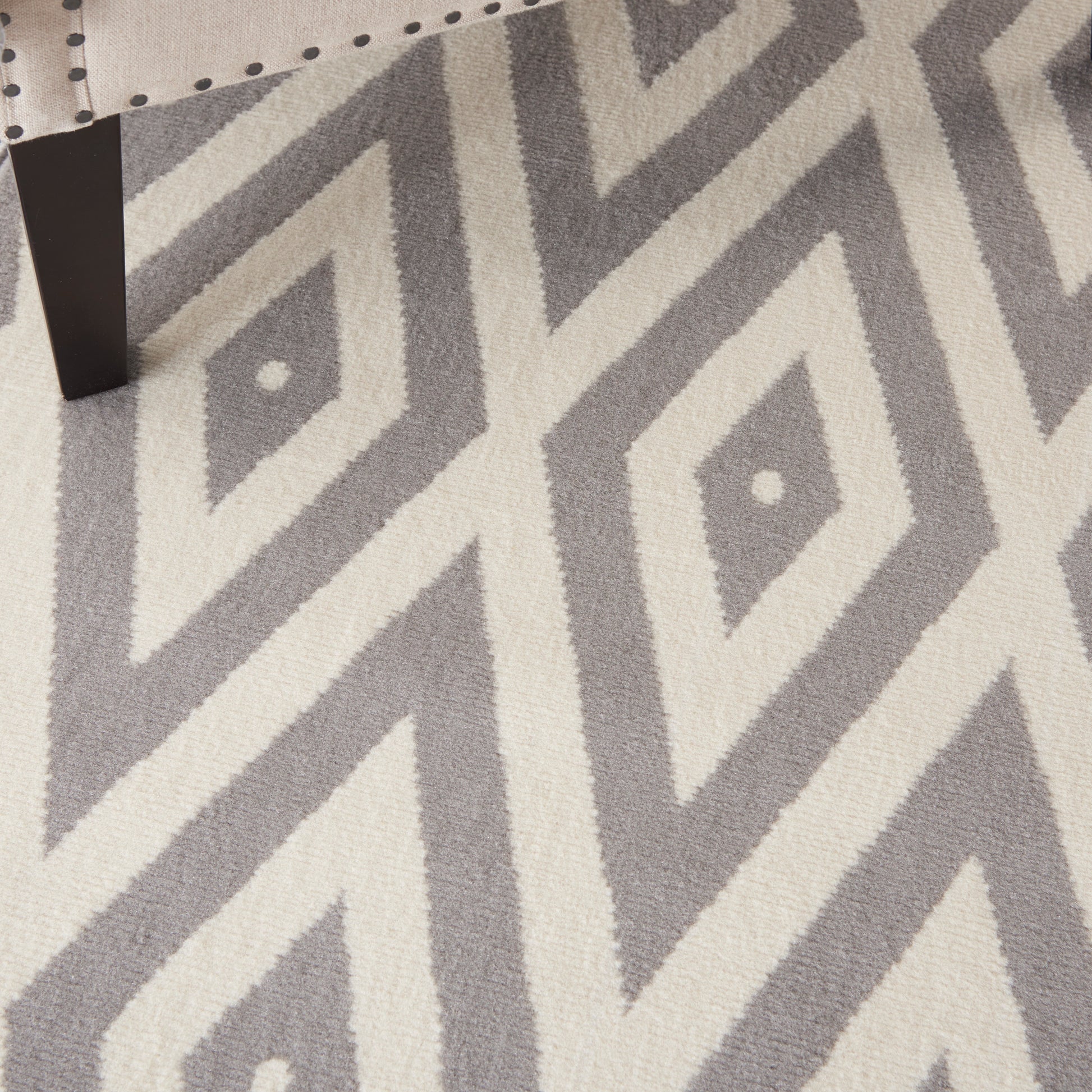 Gray and off-white geometric diamond rug with bold zigzag pattern; black chair leg visible in corner.