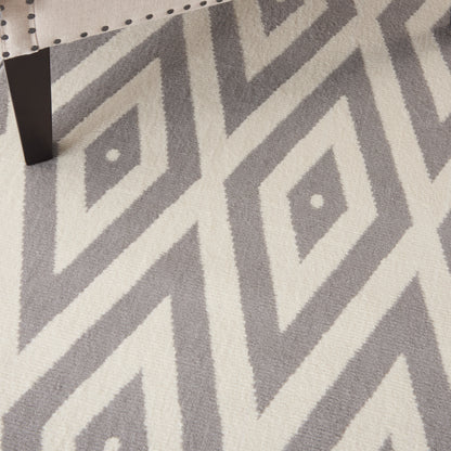 Gray and off-white geometric diamond rug with bold zigzag pattern; black chair leg visible in corner.