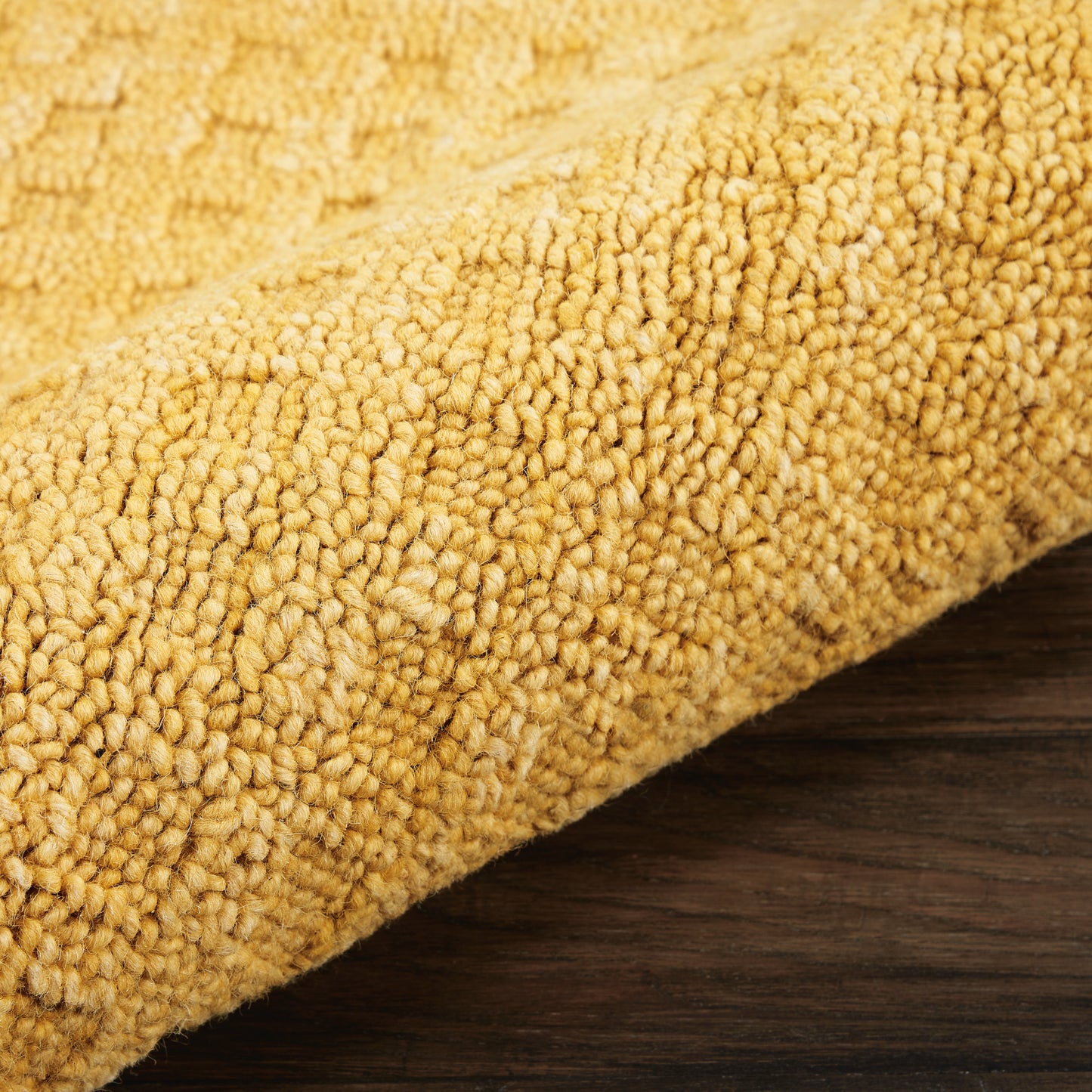 Golden yellow textured runner rug with dense plush loops, rolled on dark wood floor.