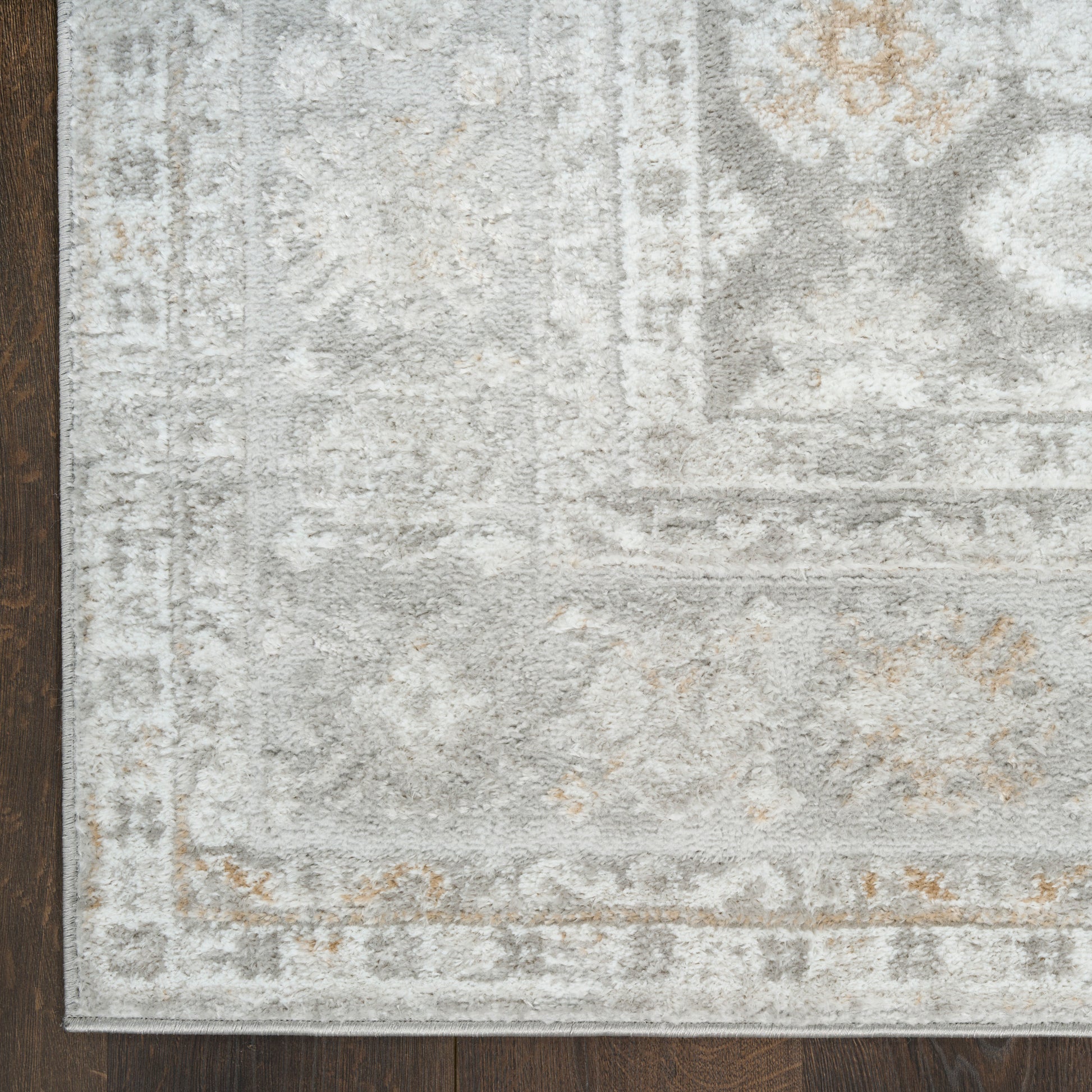 Light gray distressed area rug with ivory, beige and gold accents in a traditional pattern on dark wood floor.