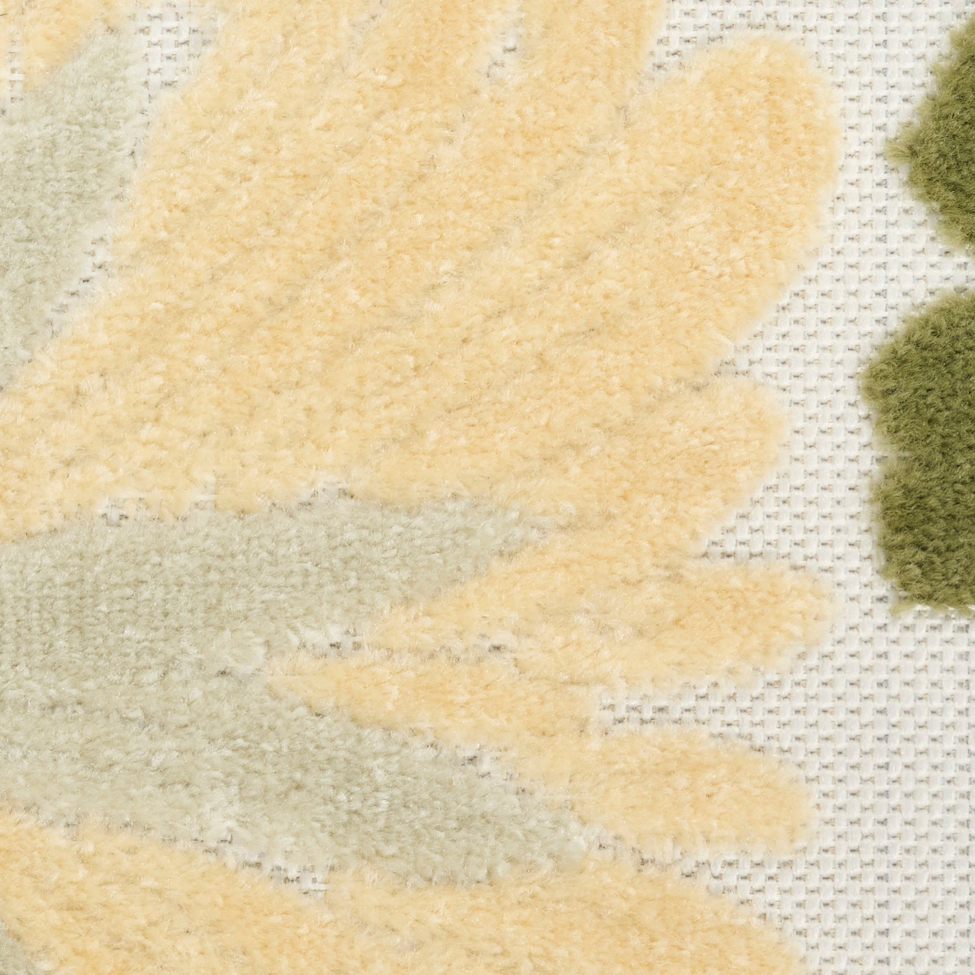 Close-up of a plush rug with pale yellow leaf shapes and olive-green accents on a light textured background.