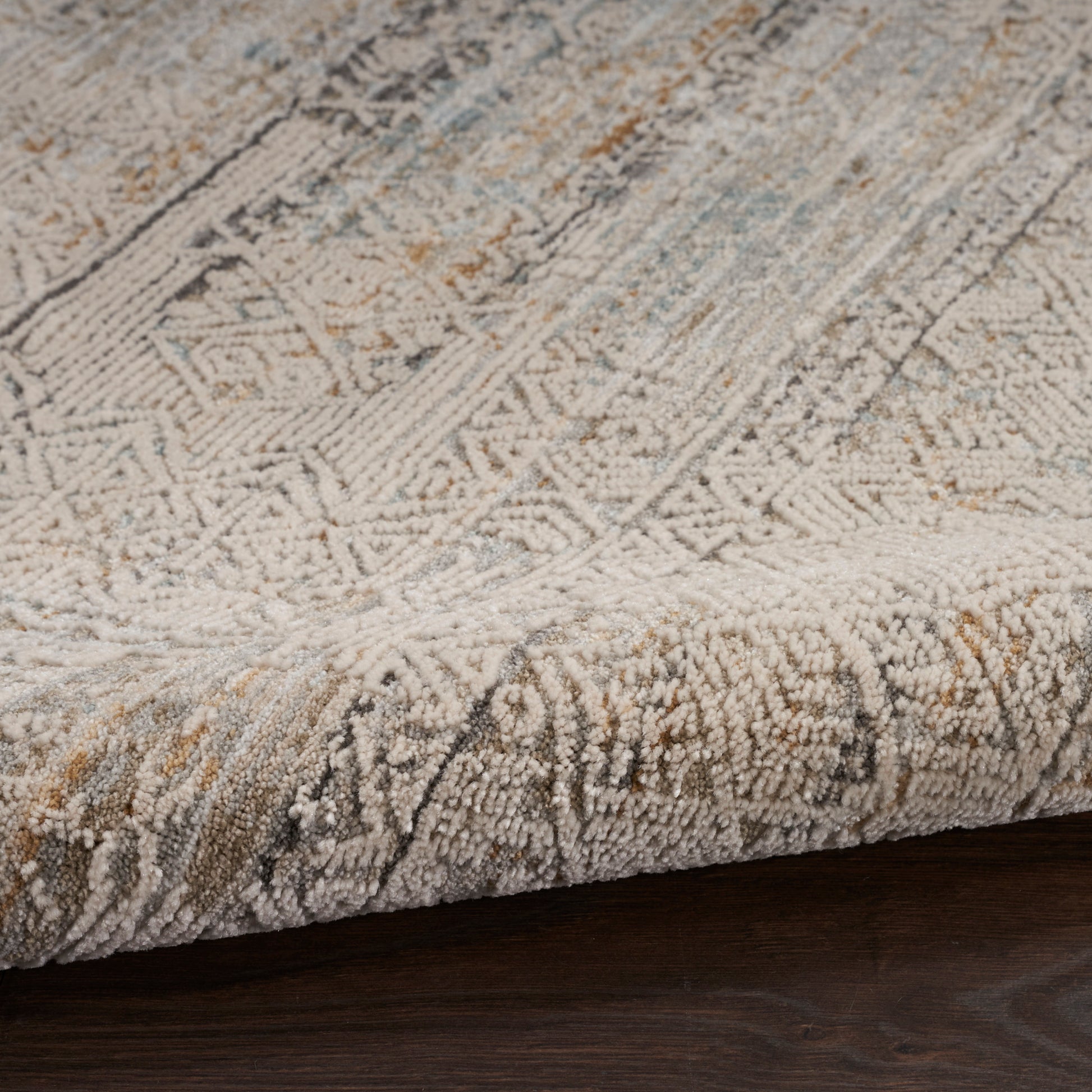 Cream and taupe geometric patterned area rug with plush pile and folded edge on dark wood floor.
