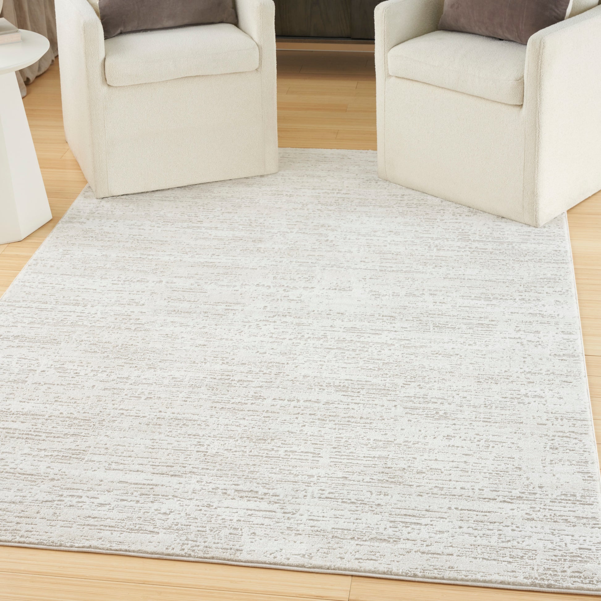 Cream upholstered armchairs flank a subtle textured beige area rug on a wooden floor.