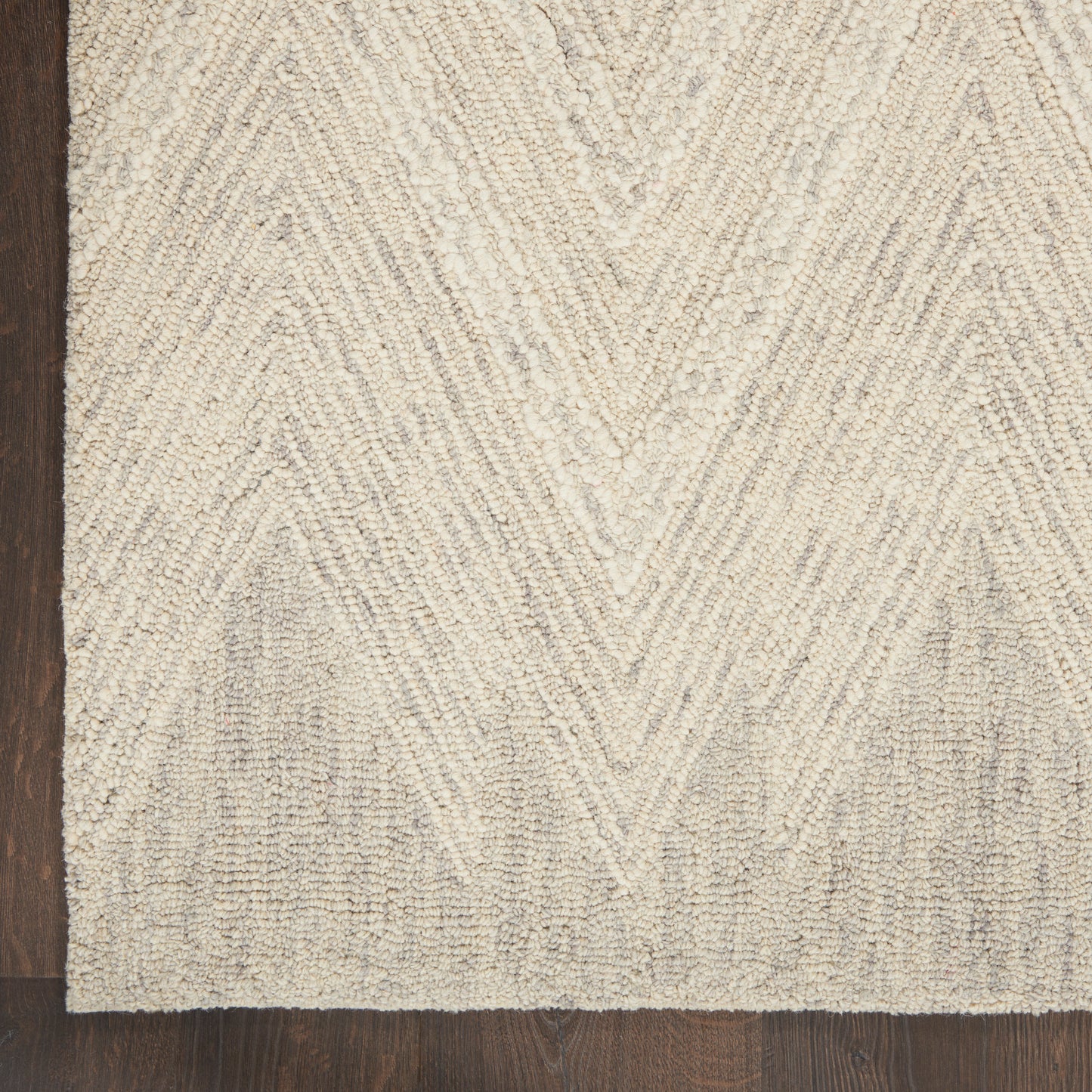 Beige textured rug with raised chevron pattern on dark wood floor.