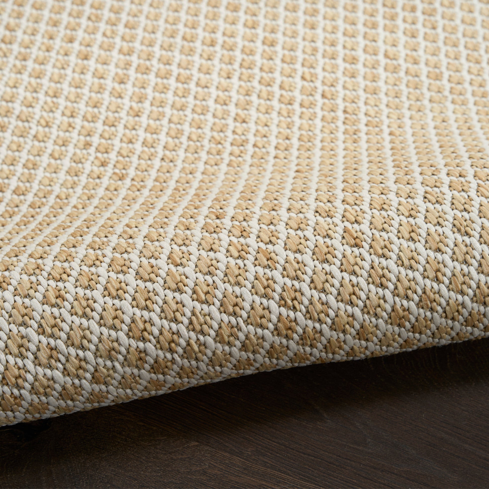 Beige and ivory woven rug with a chunky textured pattern, edge visible on dark wood floor.