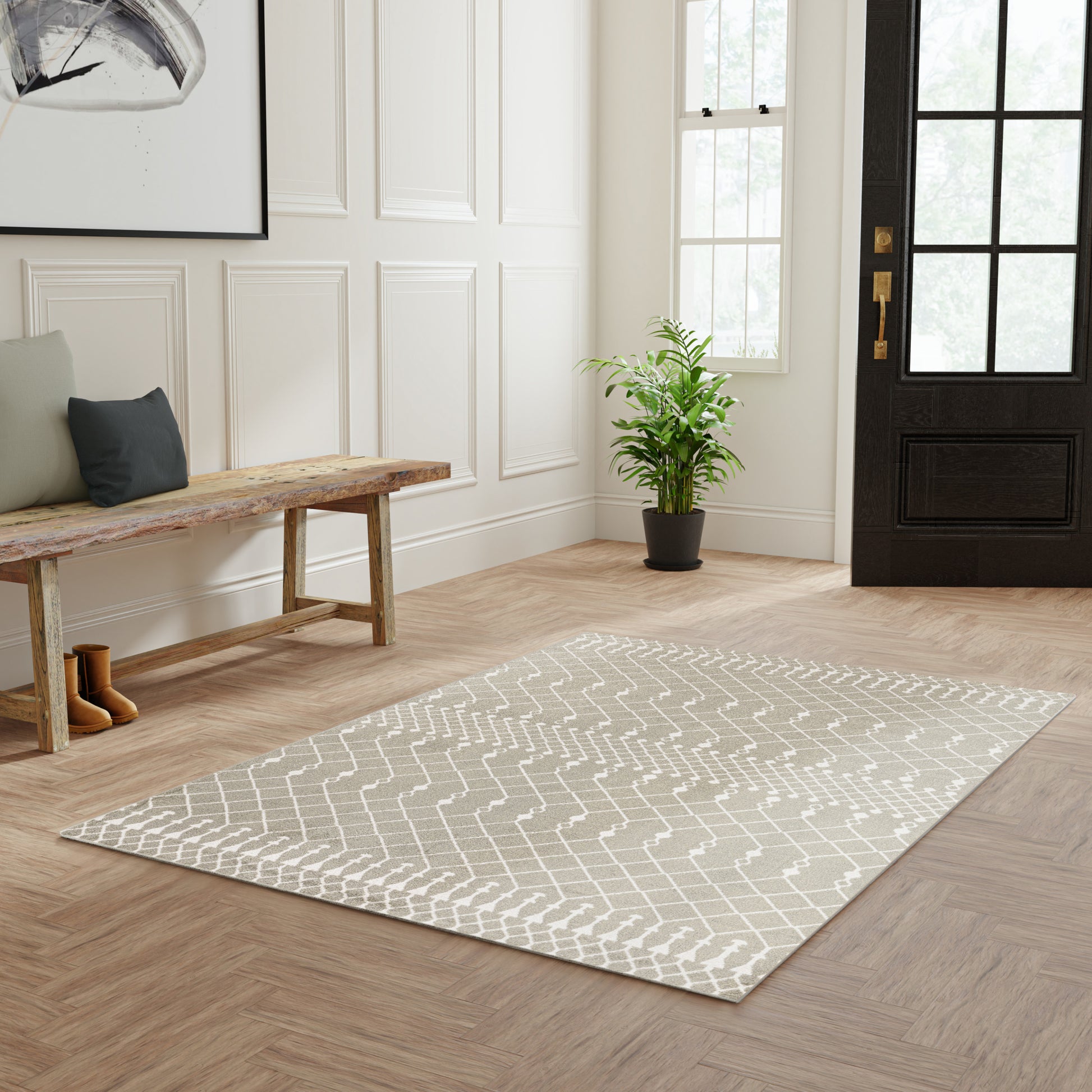 Light gray geometric-pattern area rug in entryway, wood floor, bench, potted plant, black front door with glass panes.
