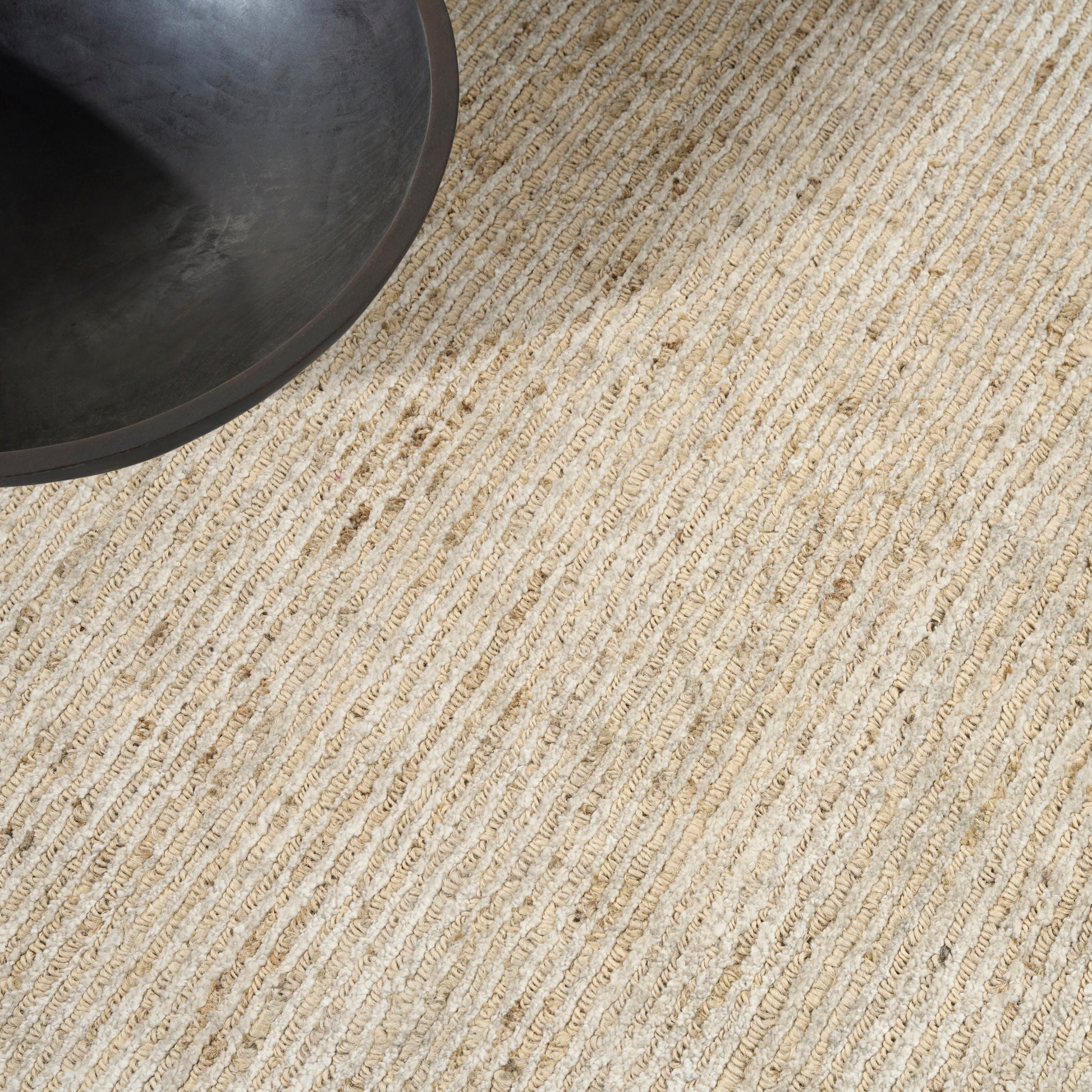 Round dark metal pan edge resting on a beige striped woven rug.