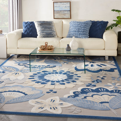 Soft blue & beige floral area rug under a cream sofa with glass coffee table & blue pillows.
