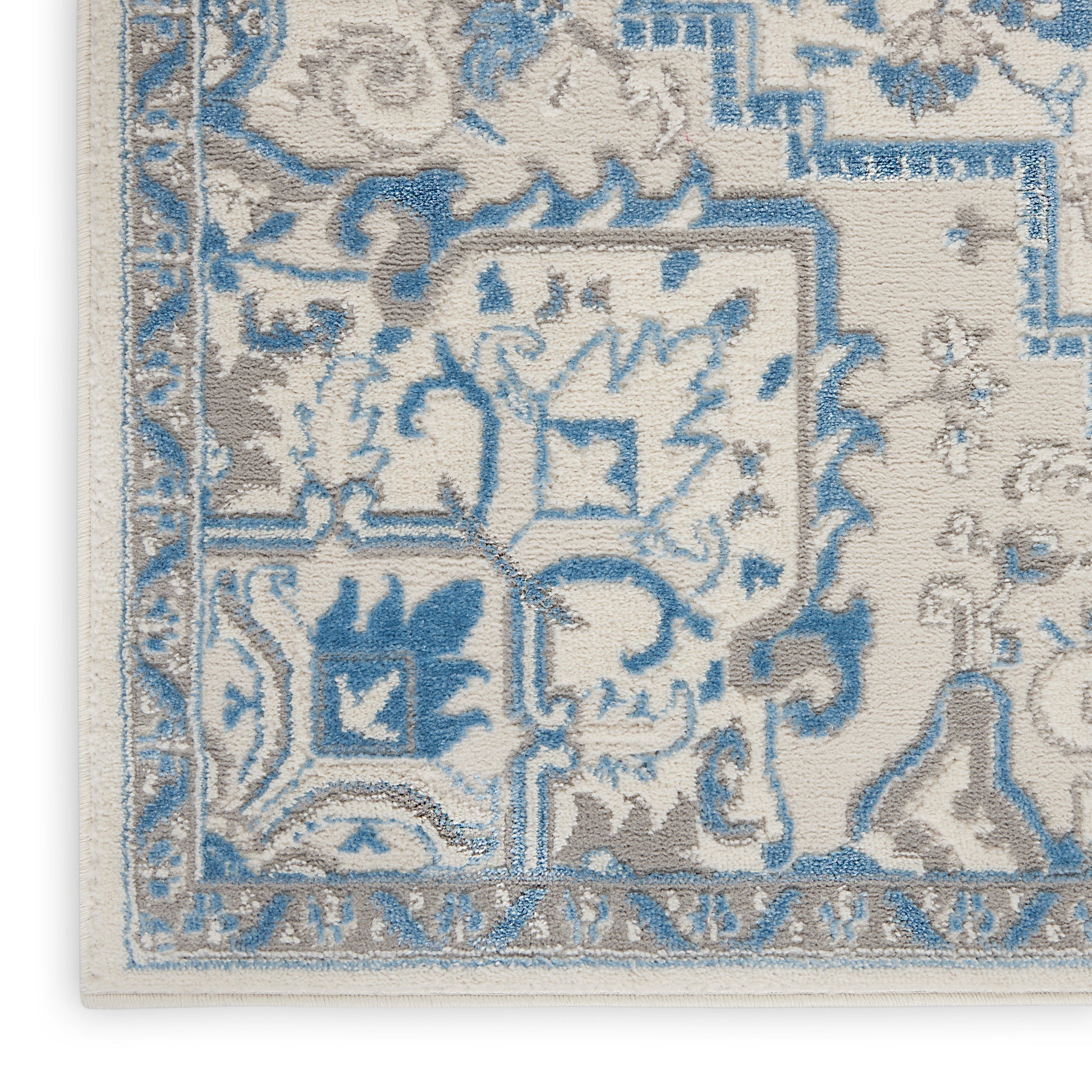 Close-up of an ornate beige and blue area rug corner with floral and geometric patterns and a detailed border.