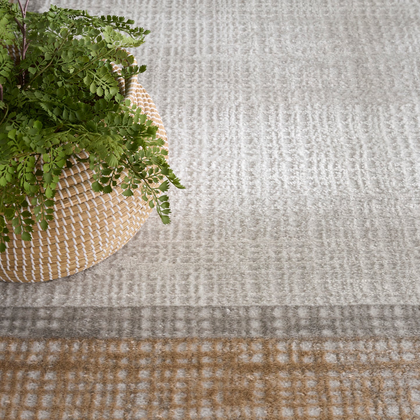 Round woven straw basket with a green fern, set on a light gray-beige textured rug