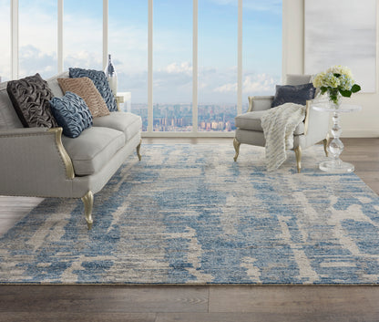 Light gray tufted sofa and matching armchair with blue abstract rug, pillows, glass side table with flowers, city view.