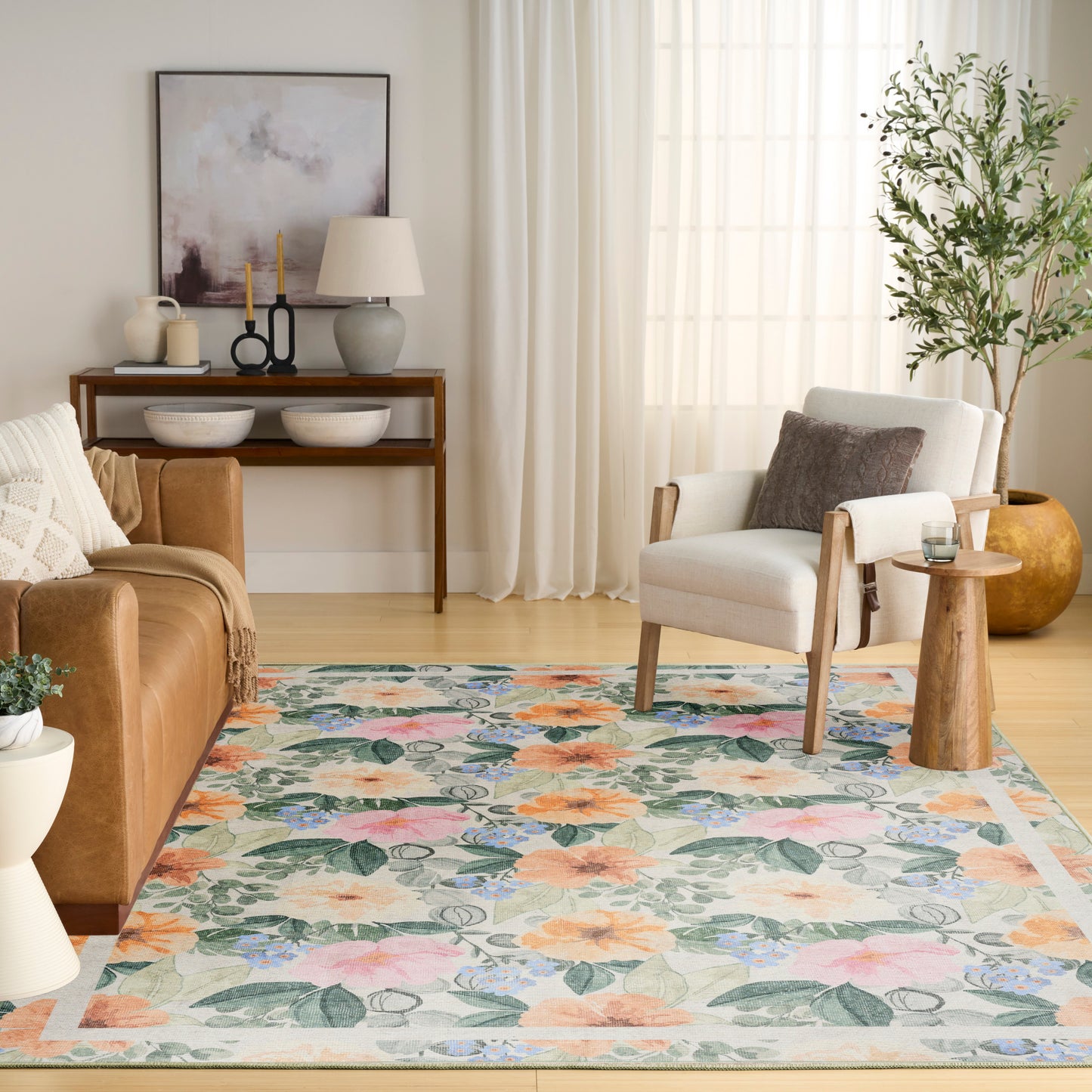 Bright living room with a colorful floral rug, brown leather sofa, white armchair, wooden side tables, and a tall plant.