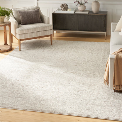 Bright living room with a large light-gray area rug, cream upholstered chairs, dark wood sideboard, and neutral decor.