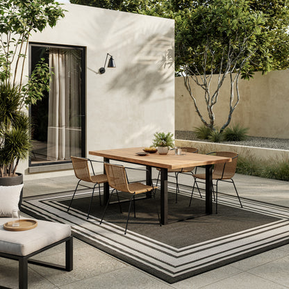 Outdoor 6' x 9' rug with black-and-white stripes on a patio, greenery in the background.