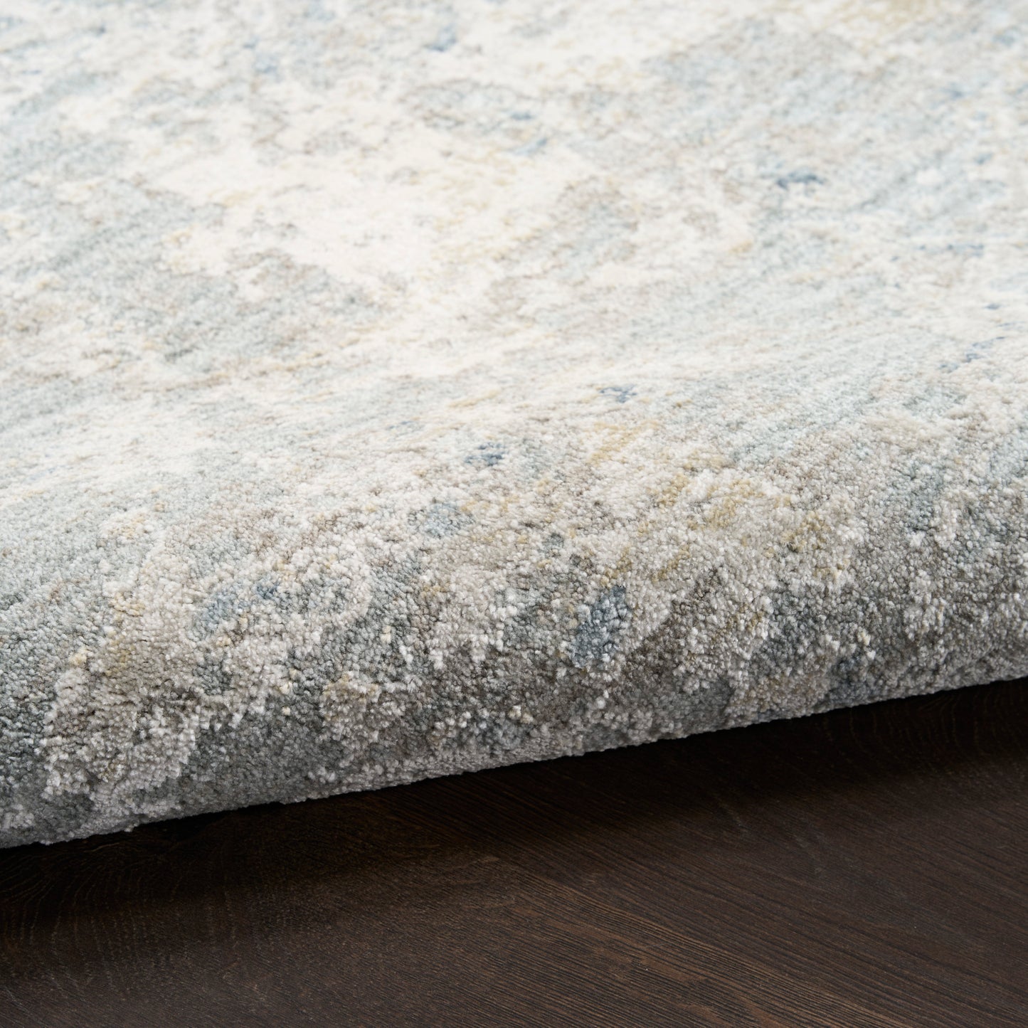 Close-up of a textured beige-blue patterned rug edge on dark wood floor.