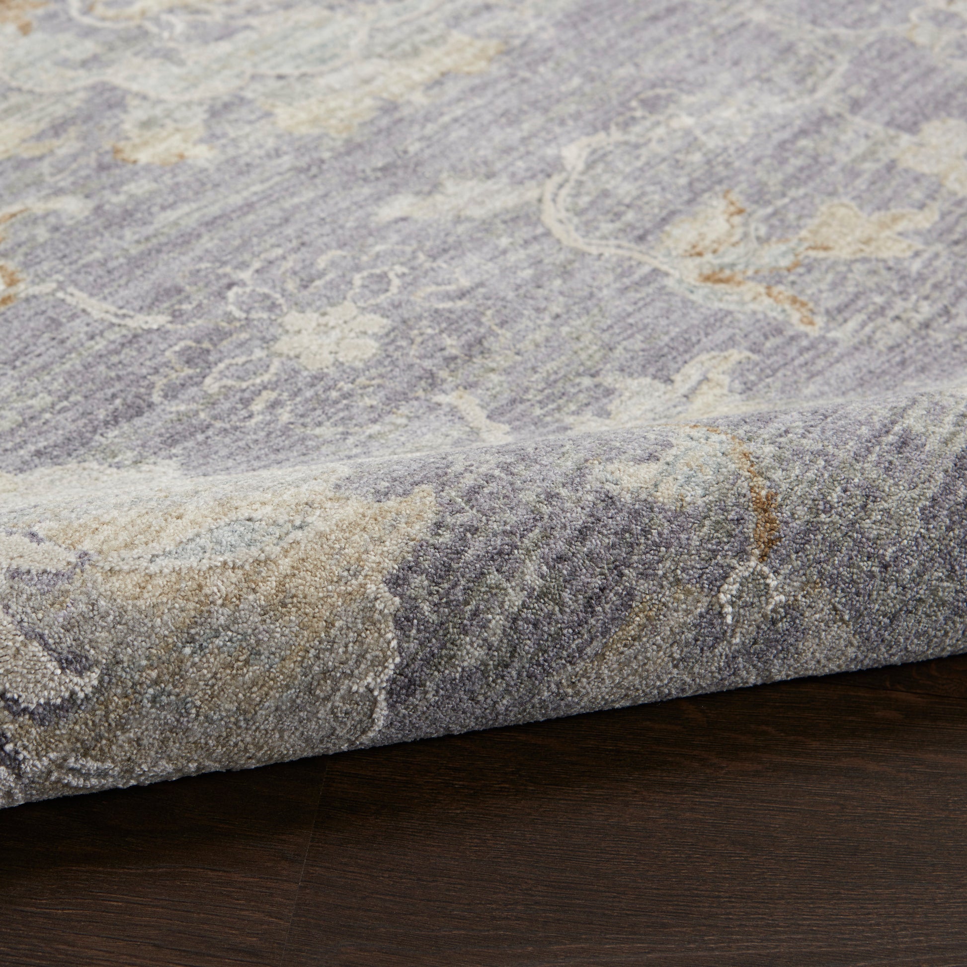 Gray-blue rug with subtle cream floral pattern, folded edge on dark hardwood floor.