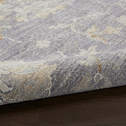 Gray-blue rug with subtle cream floral pattern, folded edge on dark hardwood floor.