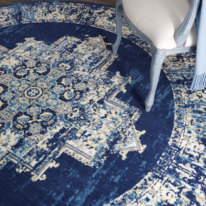Dark blue oriental rug with ivory and light blue motifs; carved gray-blue chair leg beside beige upholstered seat.